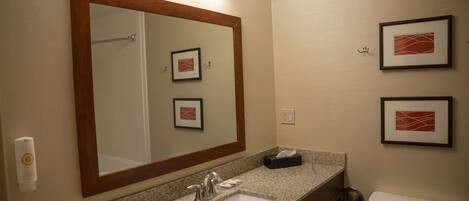Un baño con lavamanos de encimera de granito, un espejo grande, una obra de arte enmarcada en la pared y un inodoro.