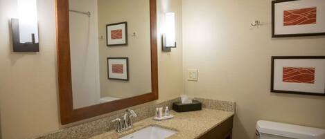 A hotel bathroom with a sink, mirror, framed pictures, and a toilet.