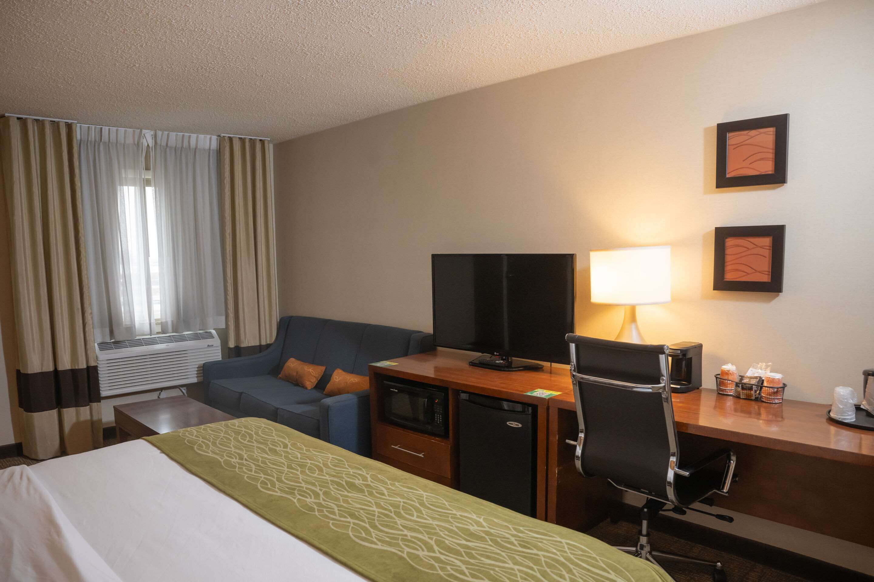 A hotel room with a bed, a desk with a computer, a television, a lamp, and a coffee maker.