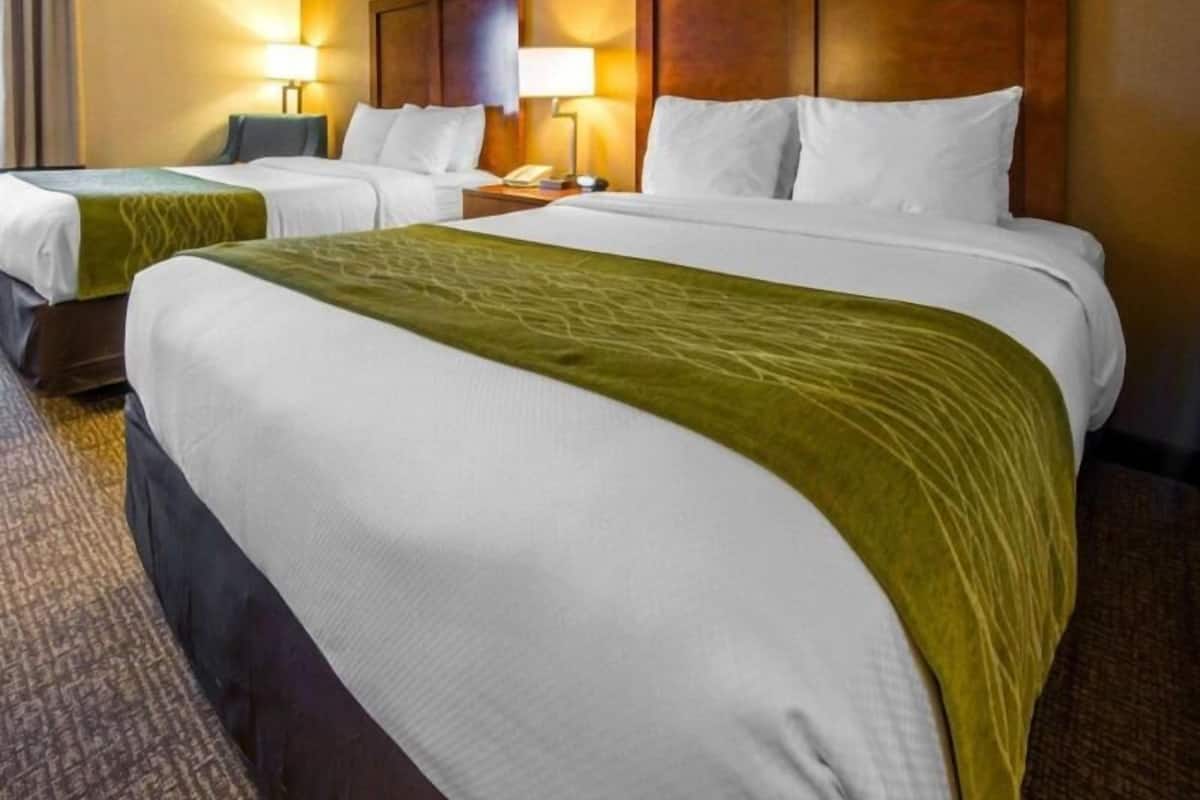 A hotel room with two beds, a wooden headboard, bedside lamps, and a carpeted floor.