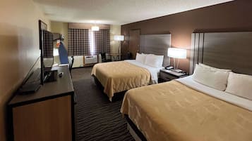 A hotel room with two beds, a desk, a chair, a TV, and a lamp.