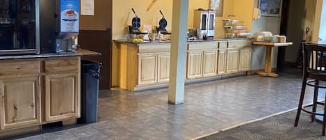 A restaurant with a counter, a refrigerator, and a coffee machine. There is a clock on the wall and a bicycle hanging on the ceiling.