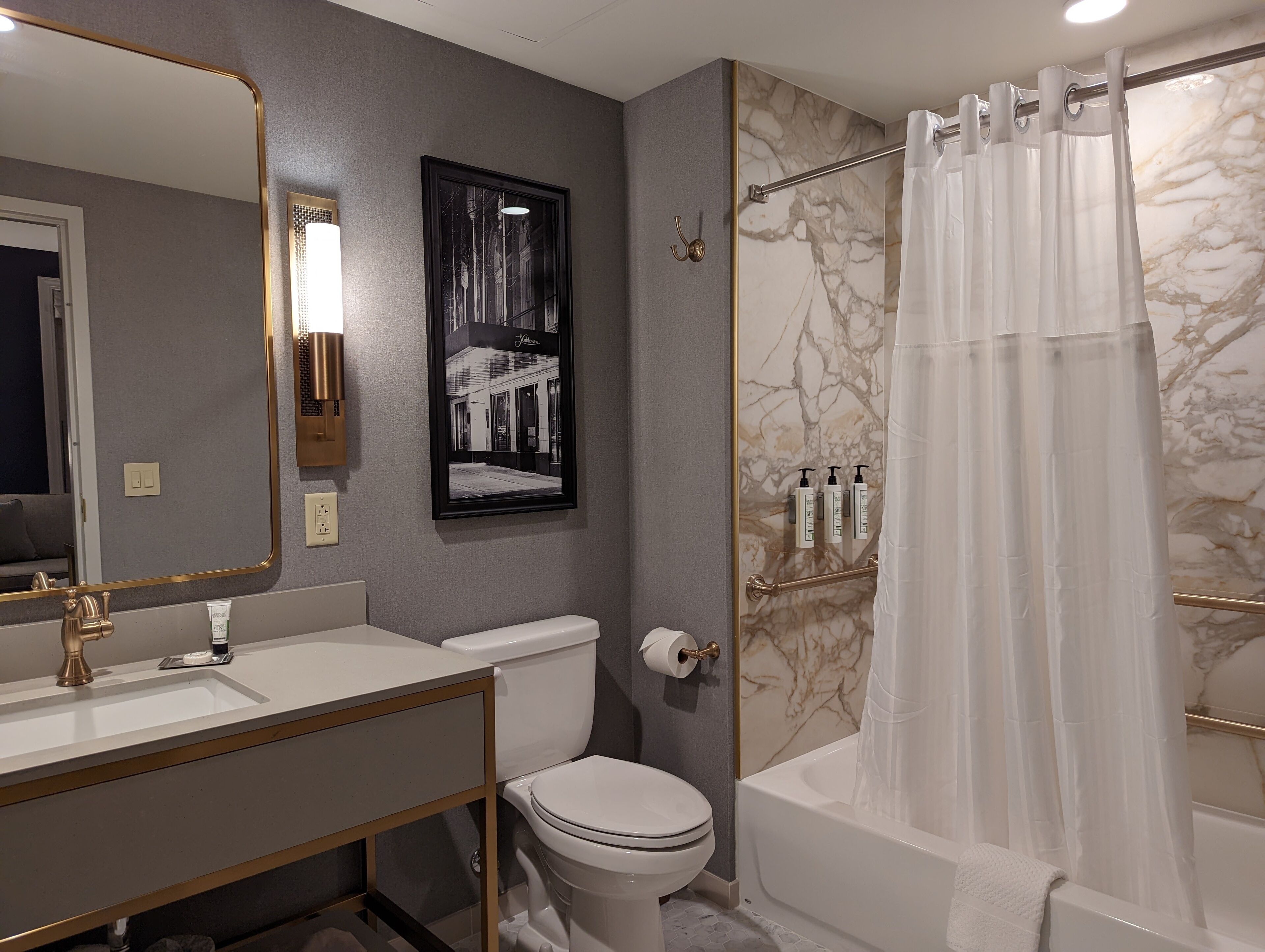 A modern bathroom with a white sink, toilet, and bathtub. There is a framed picture on the wall and a shower curtain.