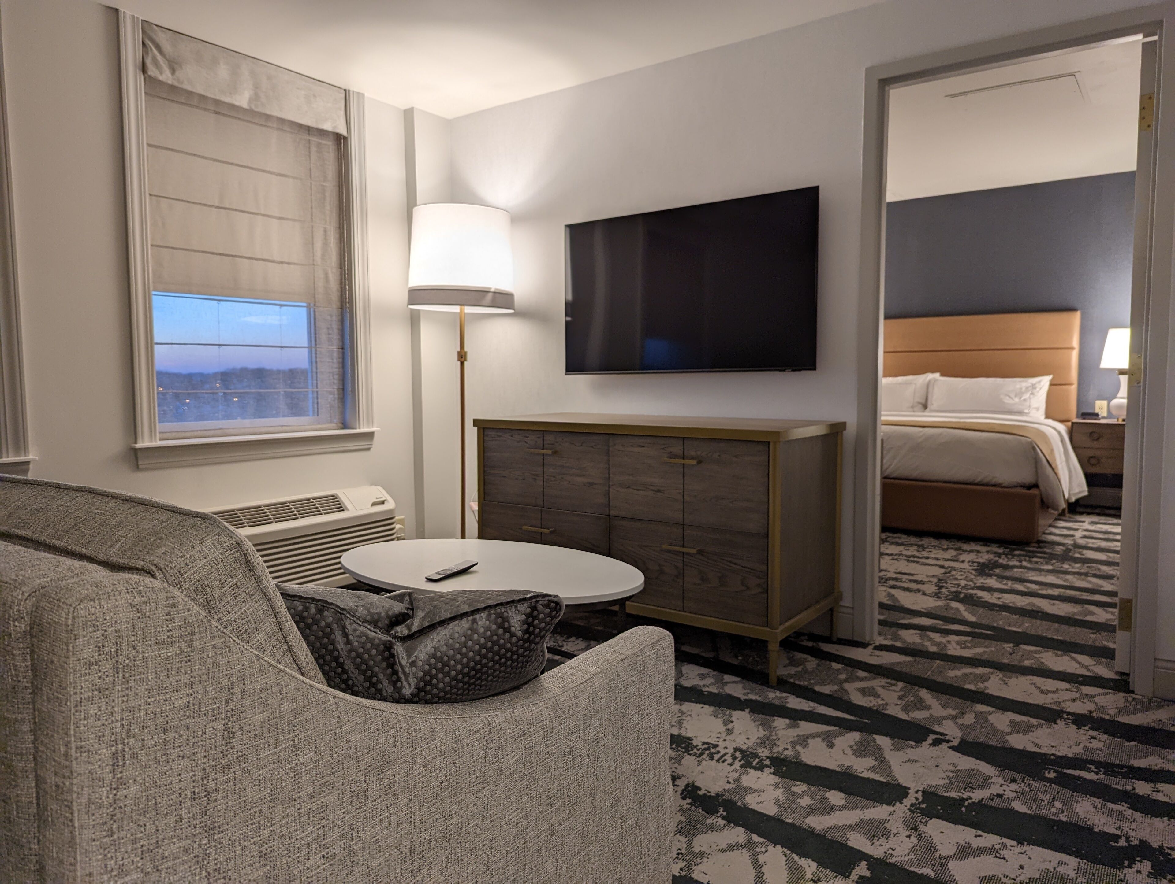 A hotel room with a bed, a TV, a desk, and a view of the city.