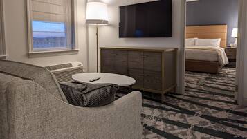 A hotel room with a bed, a TV, a desk, and a view of the city.