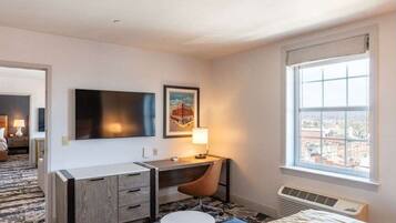 Ett hotellrum med en säng, ett skrivbord med en stol, en platt-TV, en inramad tavla, ett fönster med utsikt över staden och ett element.