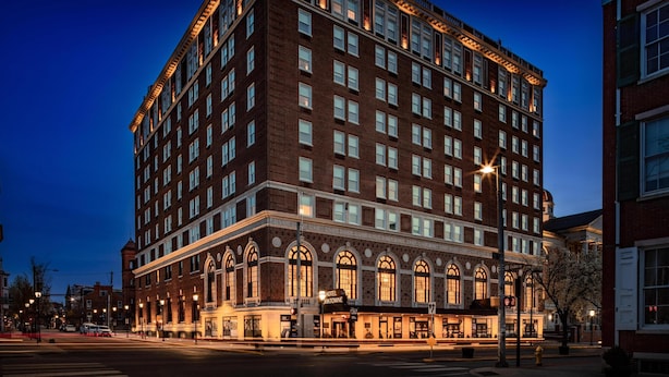 Un hotel grande de varios pisos con un estilo arquitectónico clásico, que destaca por su entrada en esquina y una bandera en la parte superior.