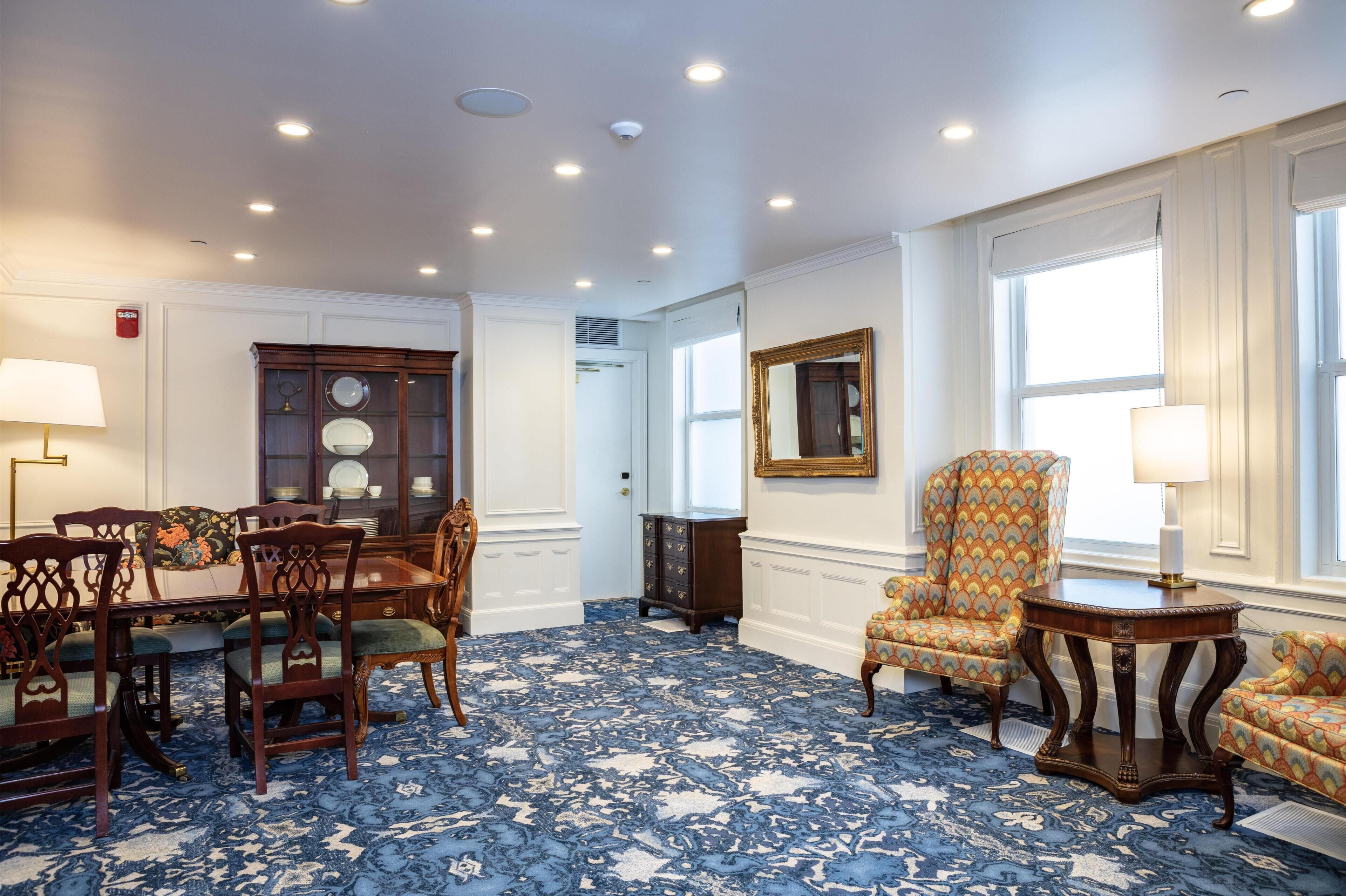 Una habitación con alfombra de diseño azul, muebles de madera, un espejo y una ventana con persianas.