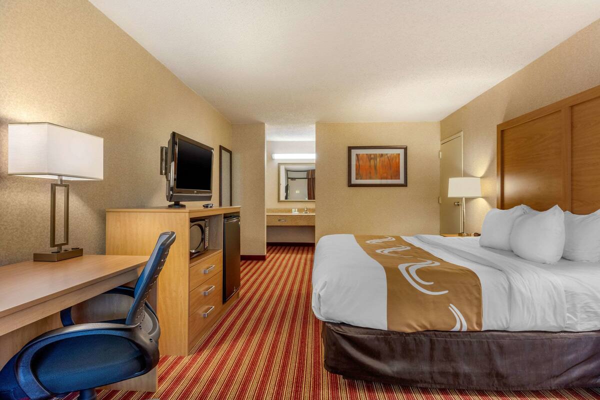 A hotel room with a bed, desk, chair, television, and a bathroom visible through an open door.