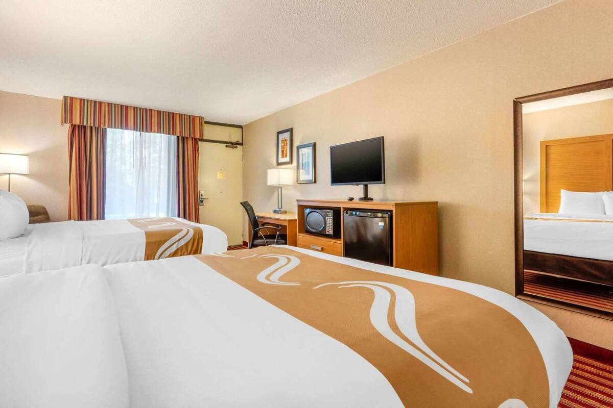 A hotel room with two beds, a desk with a television, a microwave, and a refrigerator.