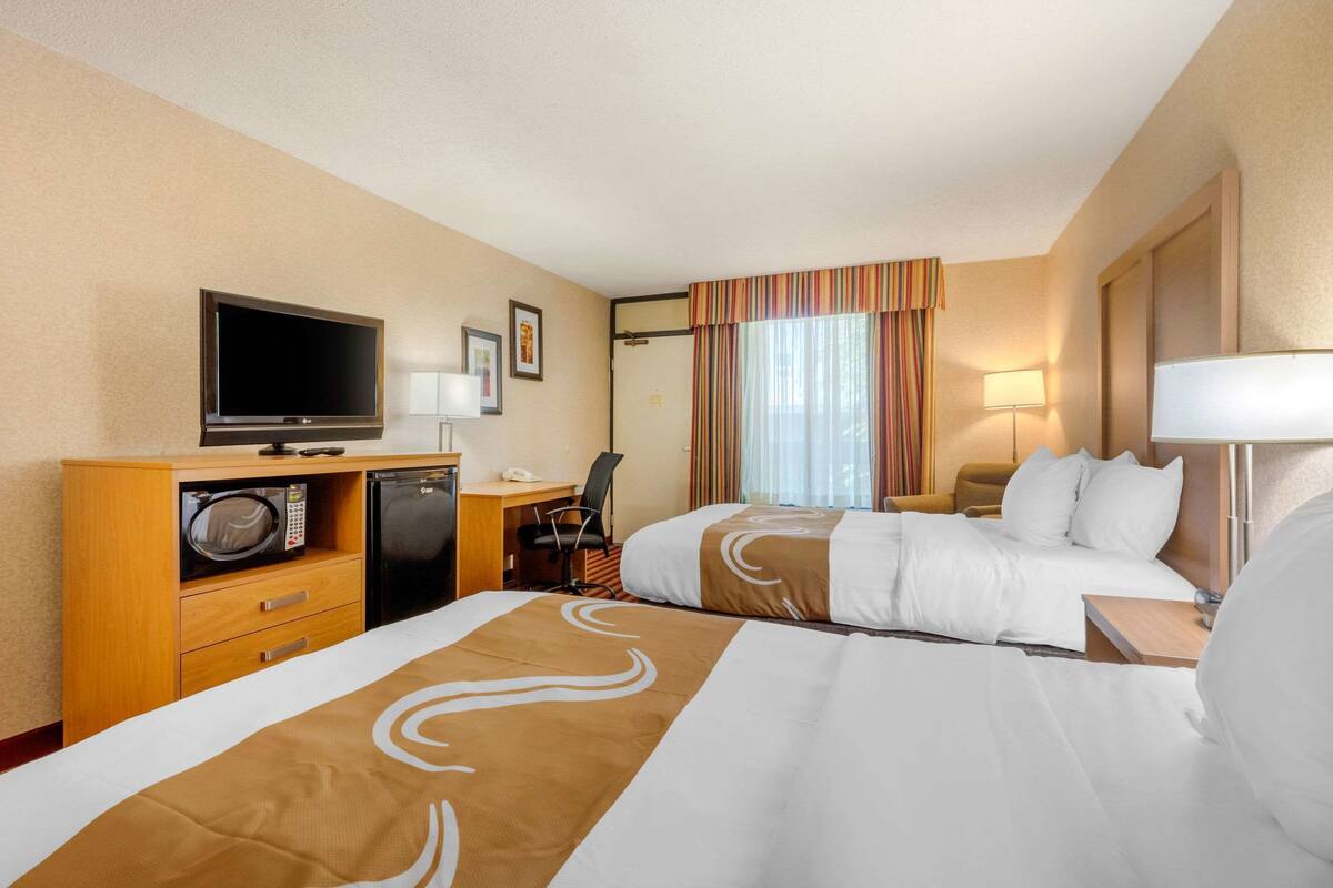 A hotel room with two beds, a desk with a computer, a television, a microwave, and a lamp.