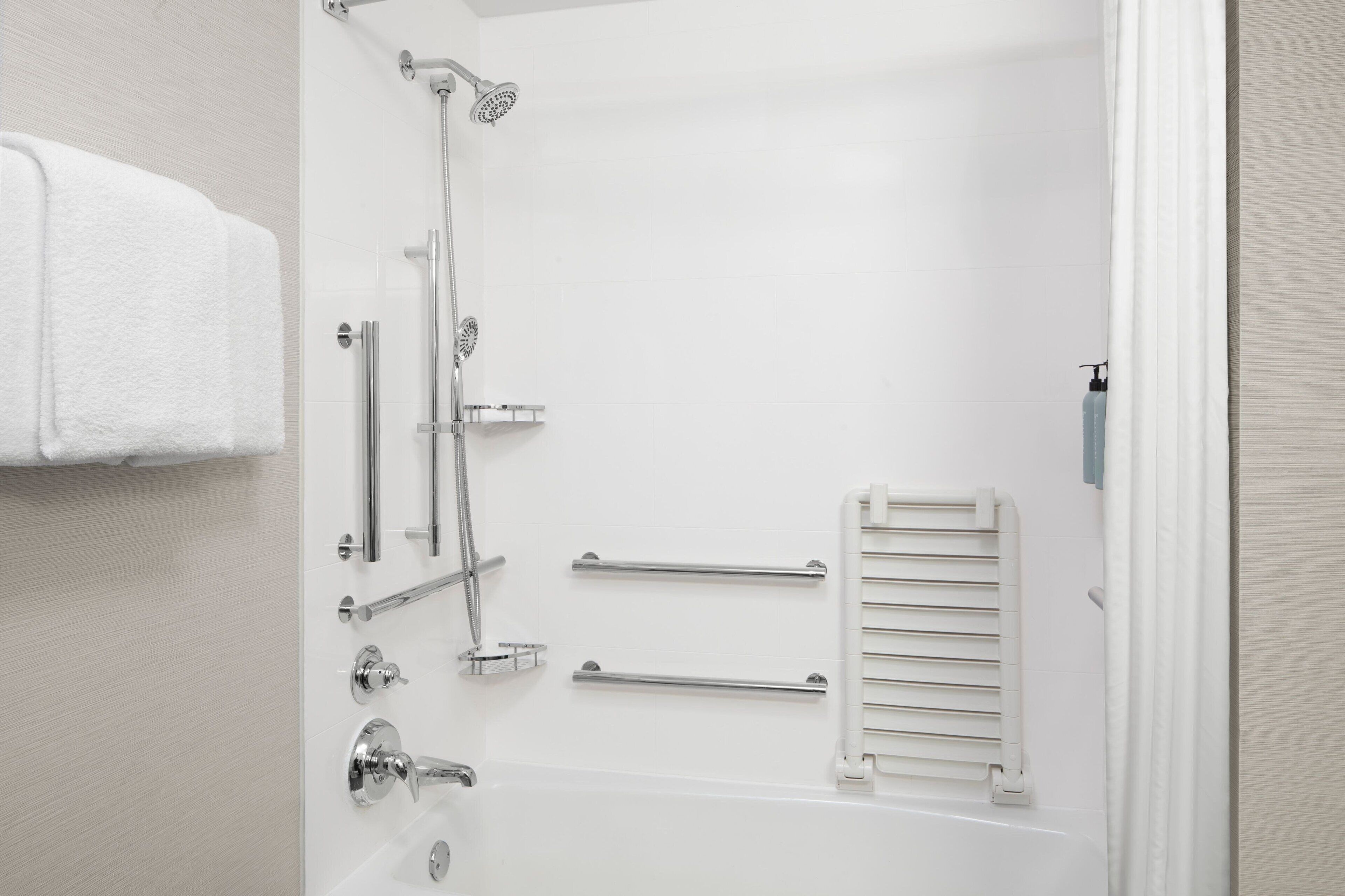 A modern bathroom with a walk-in shower, grab bars, a towel rack, and a handheld showerhead.