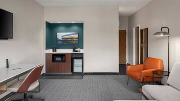 A modern hotel room with a desk, chair, sofa, and a television mounted on the wall.