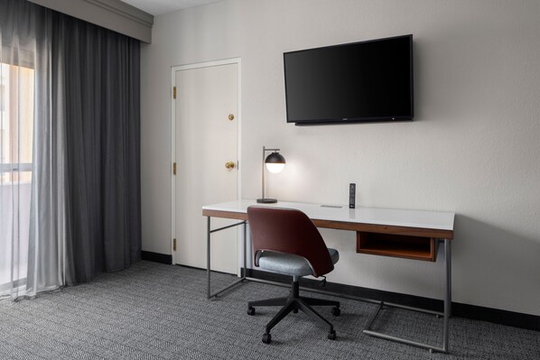 A hotel room with a desk, chair, TV, and a door. - Courtyard by Marriott Little Rock West (Little Rock)