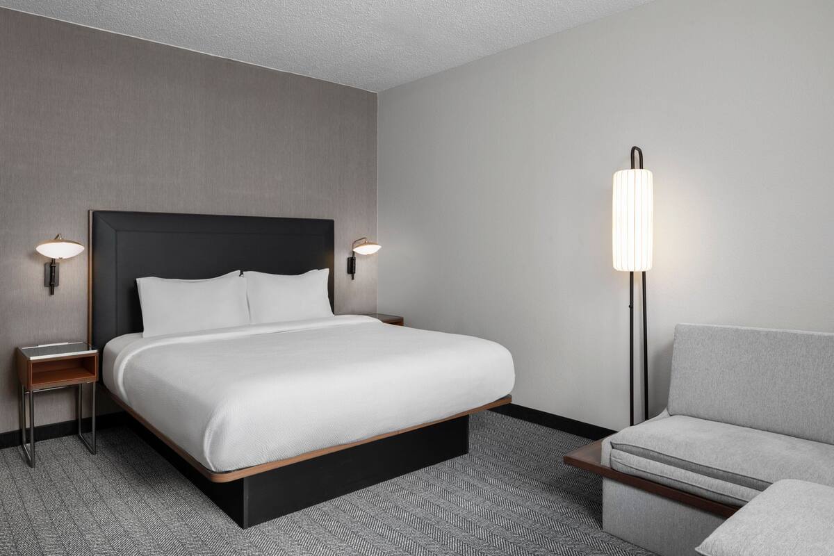 Een moderne hotelkamer met een groot bed, een nachtkastje, een stoel en een vloerlamp.
