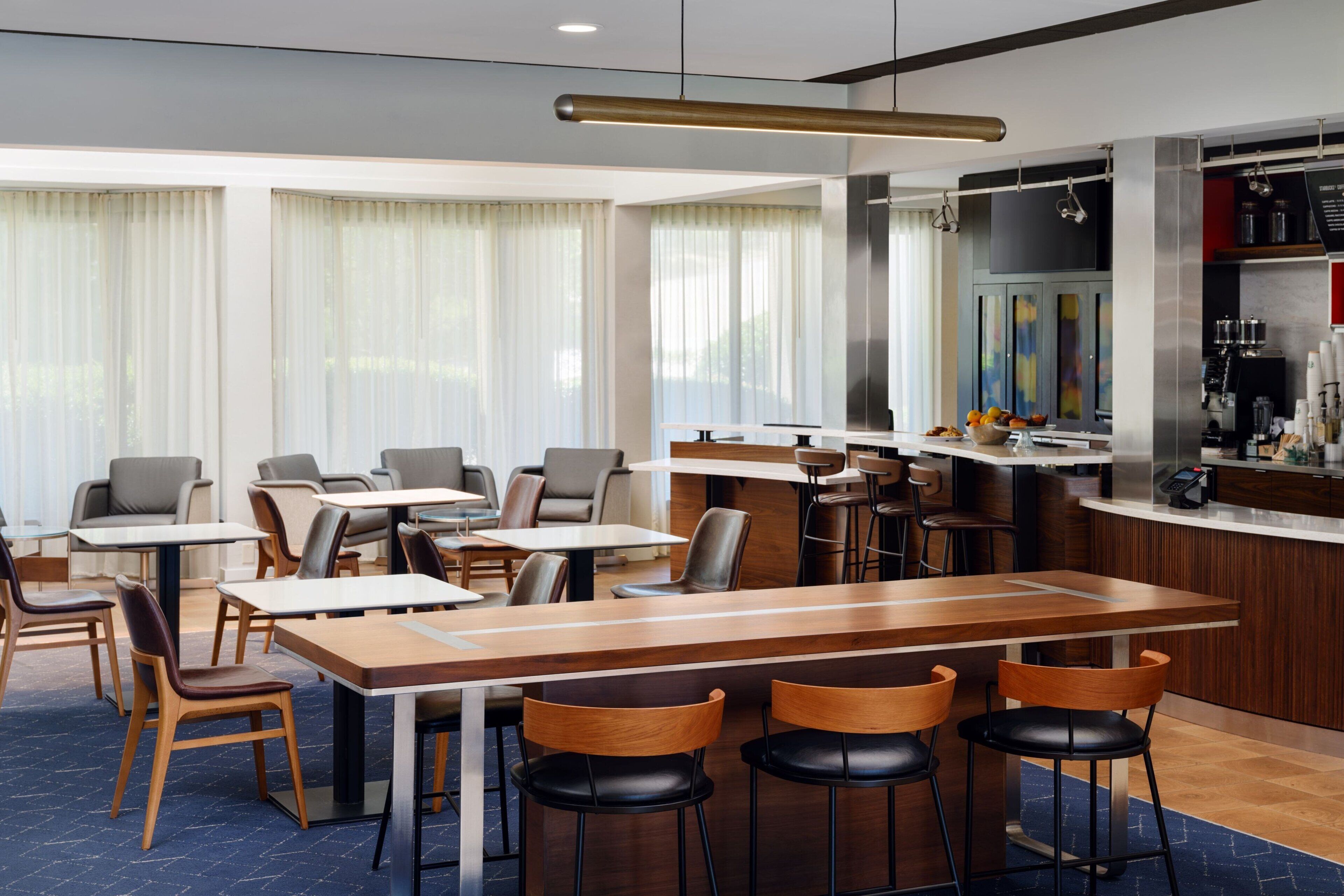 Un restaurant moderne doté de nombreuses tables et chaises, d’un bar et d’une cuisine visible au fond de la salle.