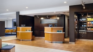 A reception area with two wooden reception desks, a seating area with yellow chairs, and a snack bar with microwaves and snack packages. - Courtyard by Marriott Little Rock West (Little Rock)