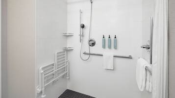 A modern shower area with a handheld showerhead, a wall-mounted faucet, and a glass-enclosed shower stall. There are two white towels hanging on a towel rack, and a set of toiletries on the wall.
