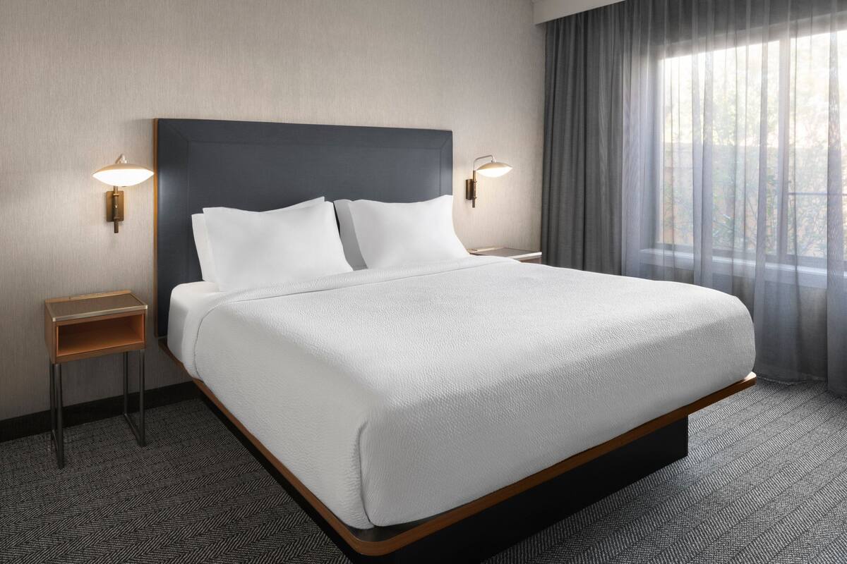 Een hotelkamer met een groot bed, twee nachtkastjes en een raam met gordijnen.