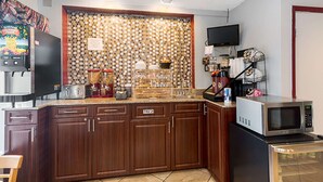 A kitchen with wooden cabinets, a microwave, a coffee maker, and a trash bin. - Magnuson Hotel Bradenton (Bradenton)