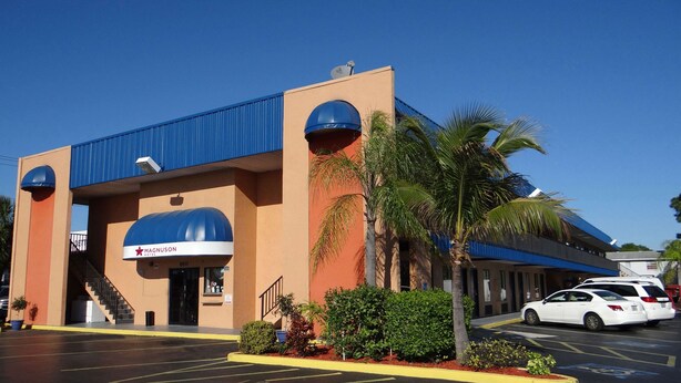 A hotel with a blue and orange exterior, a sign reading "Magnuson Hotel", and a parking lot with a white car. - Magnuson Hotel Bradenton (Bradenton)