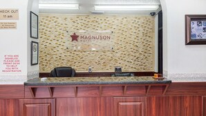 A reception desk at Magnuson Hotel with a check-out time of 11 am, a stone mosaic wall, and a sign for disabled guests. - Magnuson Hotel Bradenton (Bradenton)