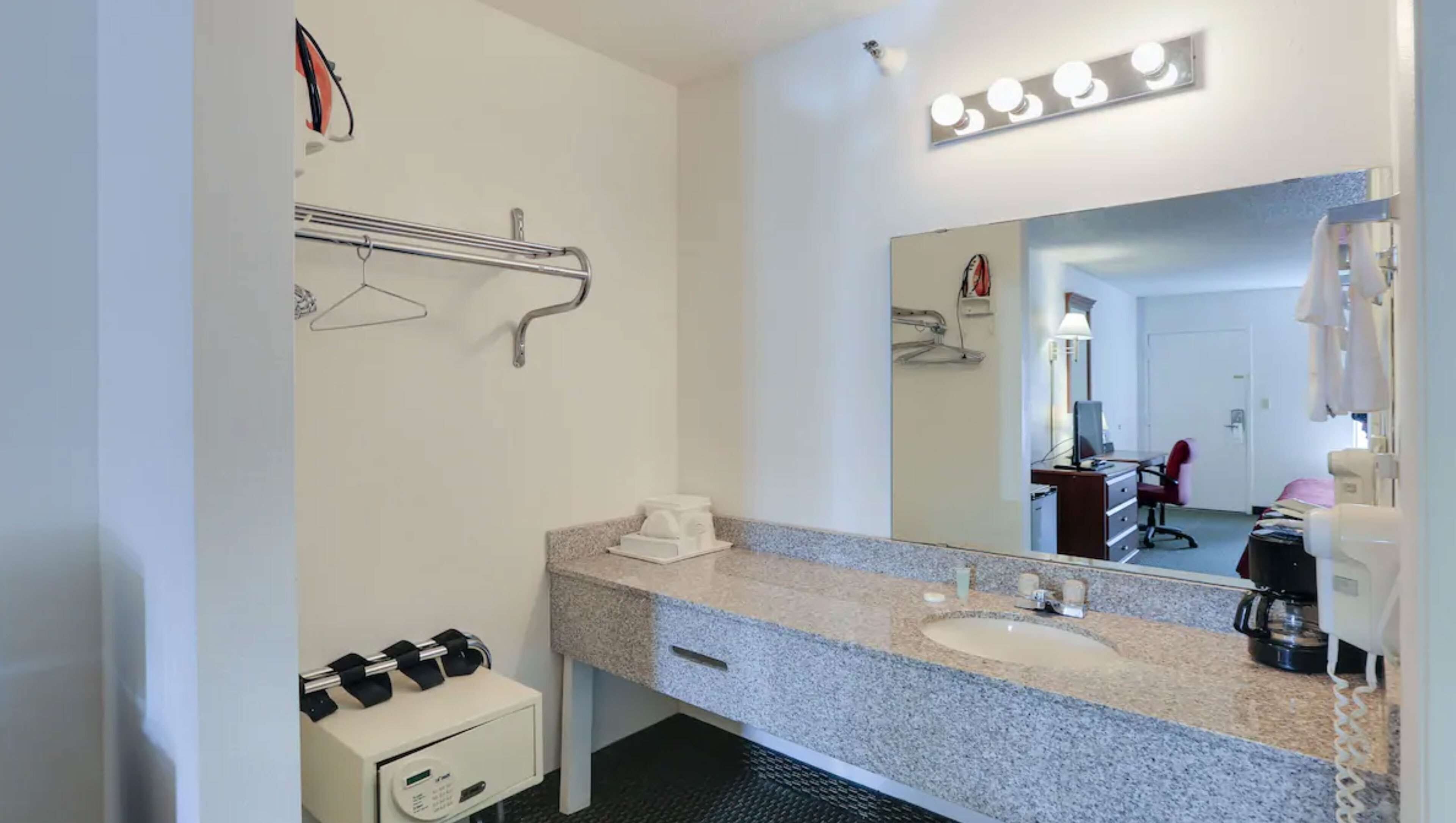 Uma casa de banho de hotel com bancada de granito, lavatório, espelho com luzes, porta-toalhas e um pequeno armário.