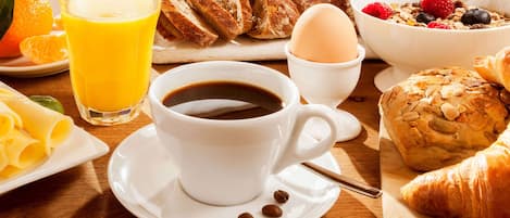 A breakfast setting with a cup of coffee, orange juice, croissants, a bowl of cereal with berries, and a plate of sliced oranges.