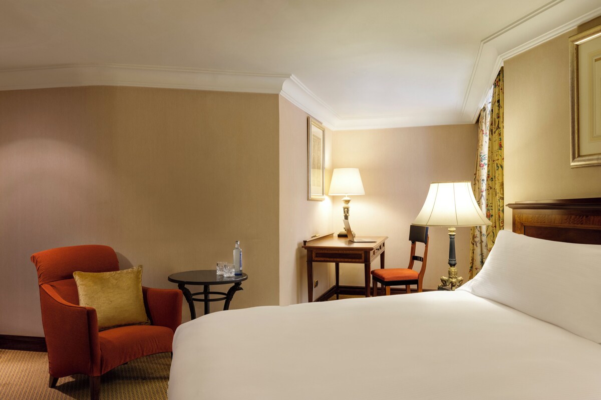 Una habitación de hotel con una cama grande, un sillón rojo, una mesita con una lámpara y una silla.