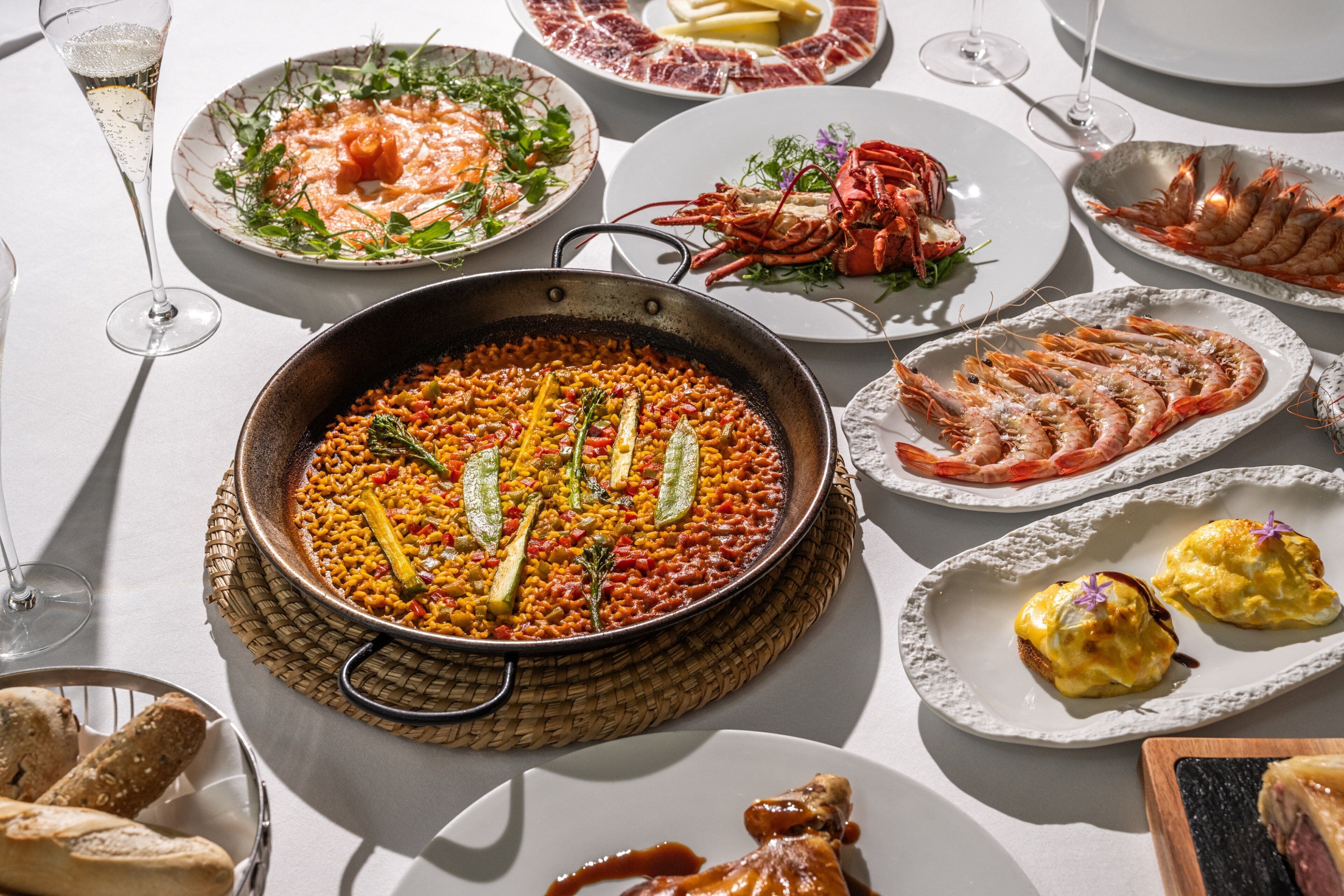 Una mesa servida con diversos platos, incluyendo mariscos y una paellera grande.