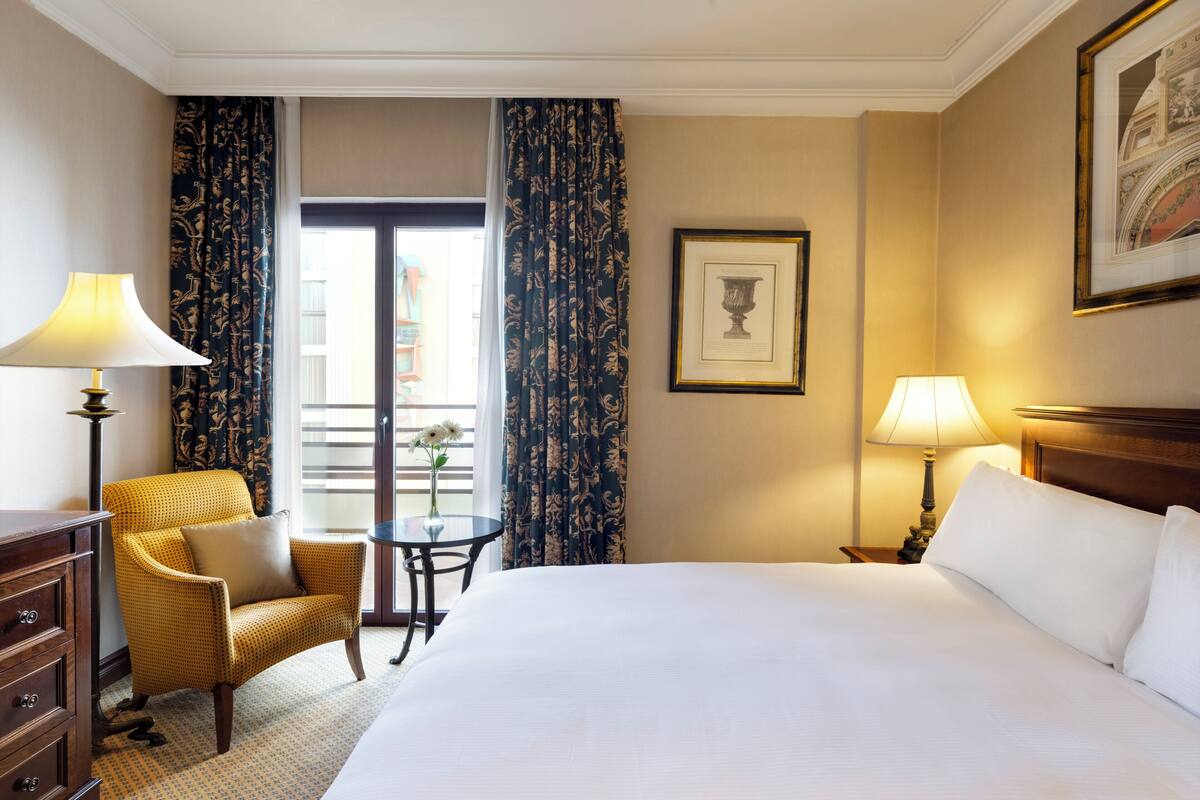 Una habitación de hotel con una cama grande, una silla, una mesita y dos lámparas.