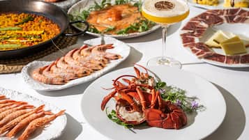 Variedad de platos de mariscos, una copa de bebida y fuentes de comida sobre una mesa.