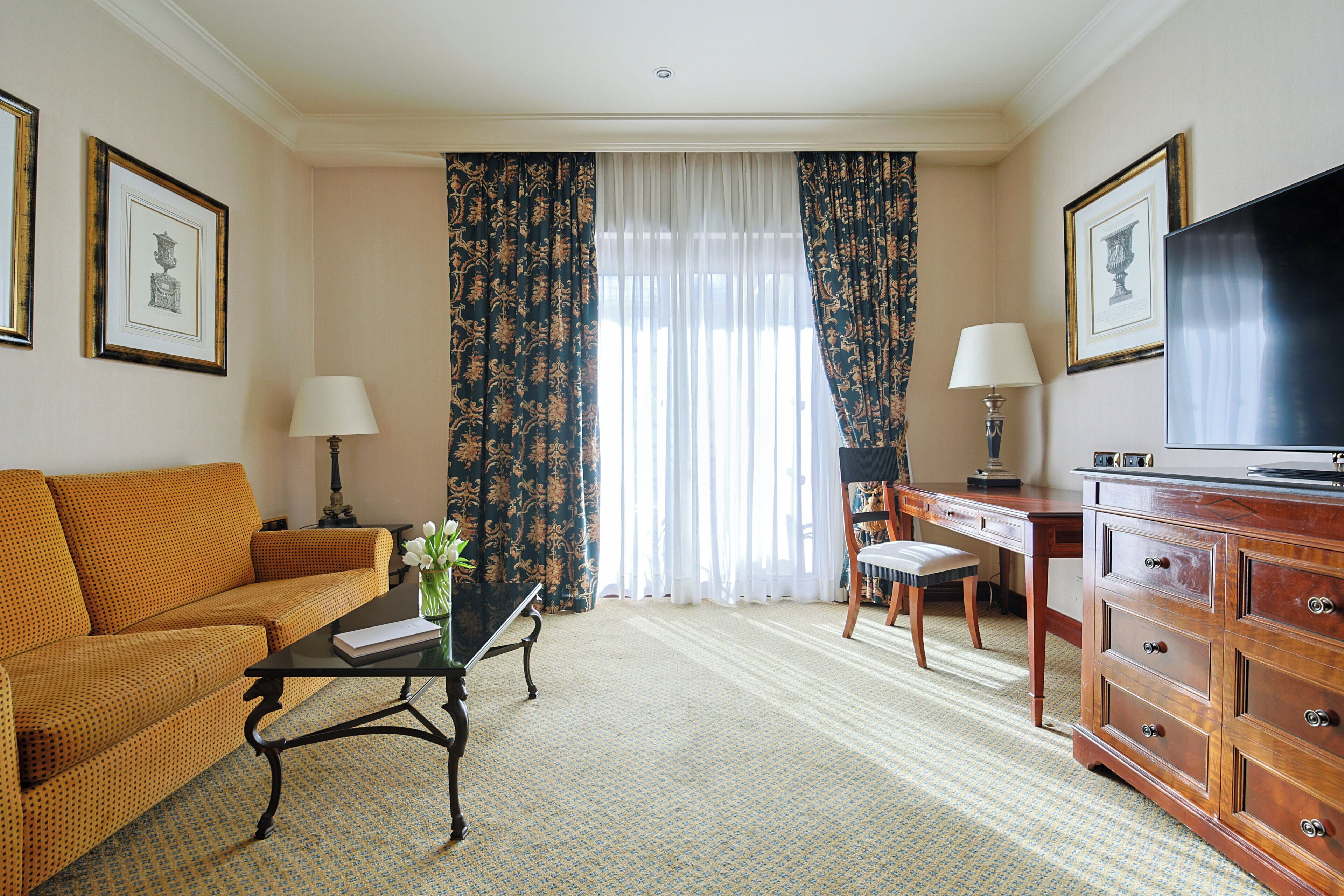 Une chambre d’hôtel équipée d’un canapé, d’un bureau, d’une télévision et d’une fenêtre avec des rideaux.