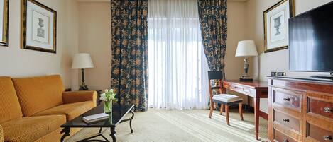 Habitación de hotel con sofá, escritorio, televisor y ventana con cortinas.