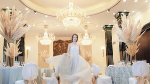 A woman in a white dress standing in a luxurious room with chandeliers, tables set for a formal event, and tall decorative plants. - InterContinental Madrid by IHG (Madrid)