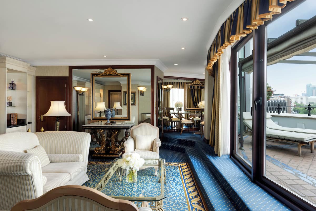 Habitación de hotel con un ventanal grande, un sofá, una silla, una mesa con un florero y un espejo.
