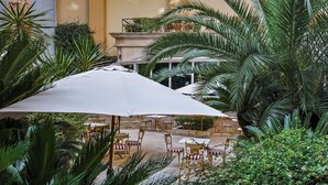 Un espace patio intérieur aménagé avec des tables et des chaises, entouré d’une végétation luxuriante et abrité par un grand parasol.