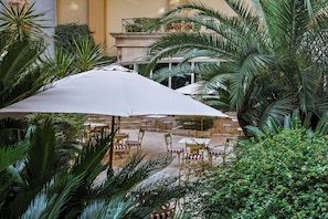 Un patio interior con mesas y sillas, rodeado de abundante vegetación y un gran paraguas.