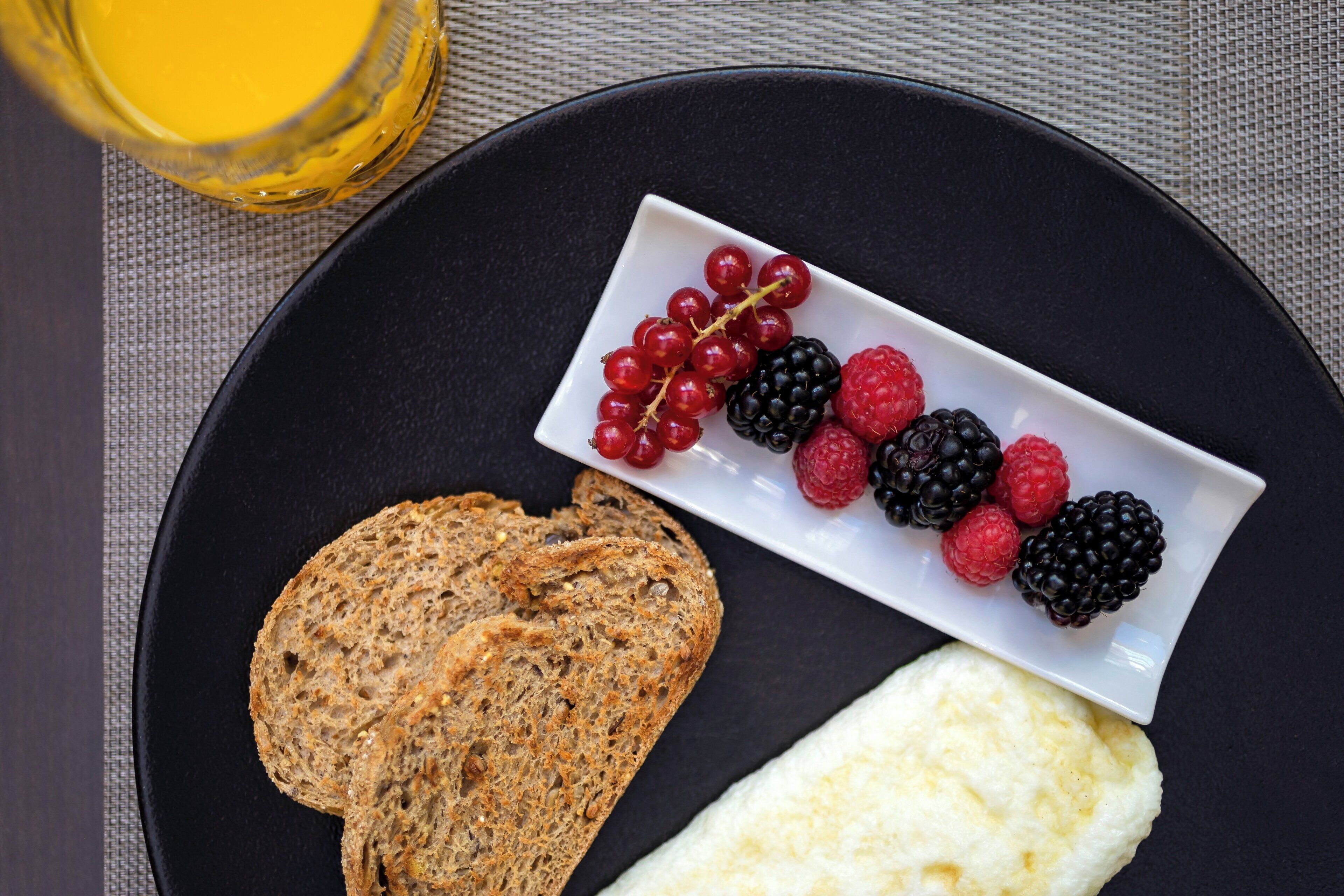Une assiette avec des tranches de pain complet, un fromage blanc et un petit bol de fruits rouges mélangés.