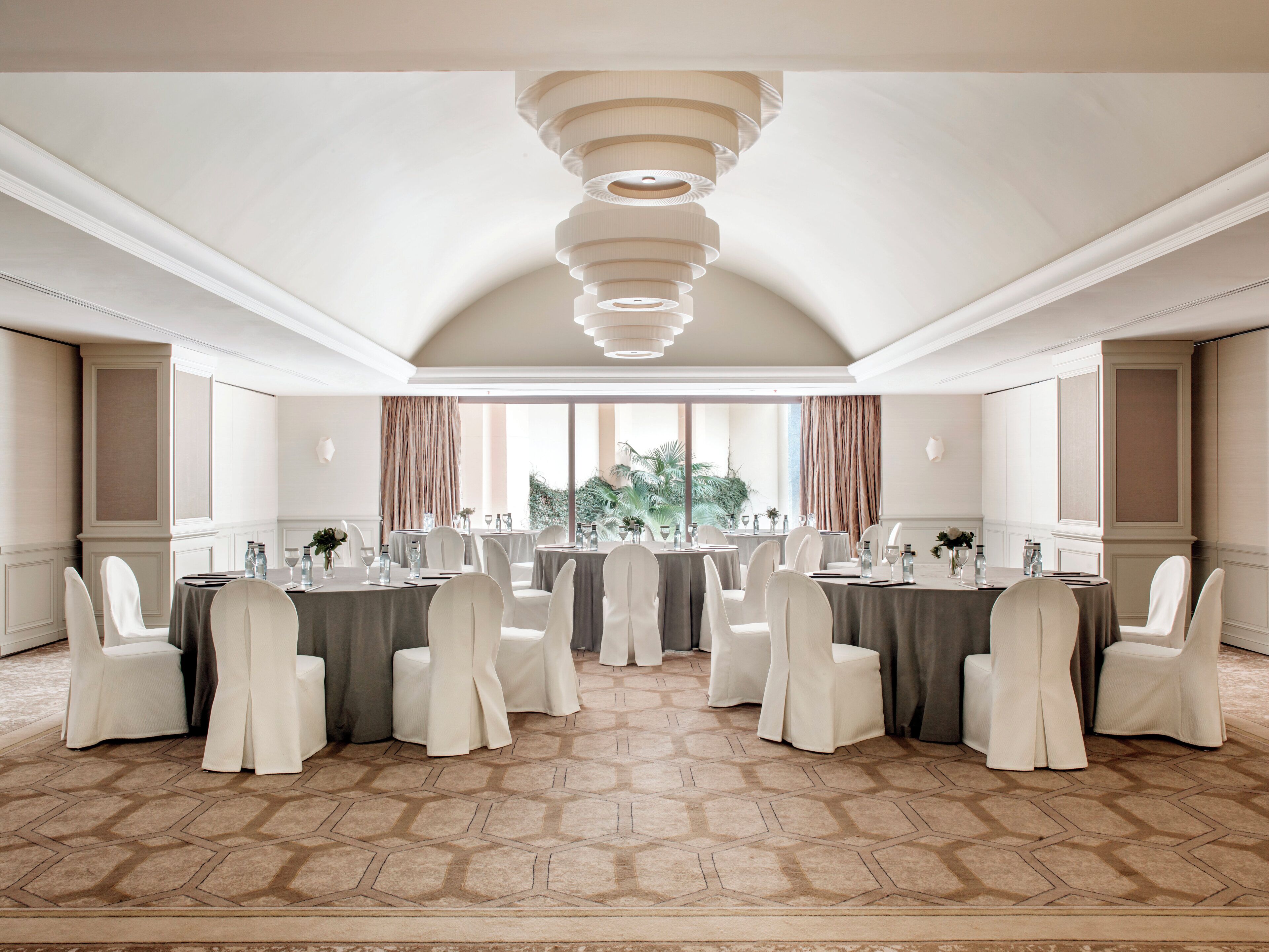 Une salle de conférence avec des tables rondes, des chaises blanches et un tapis à motifs.