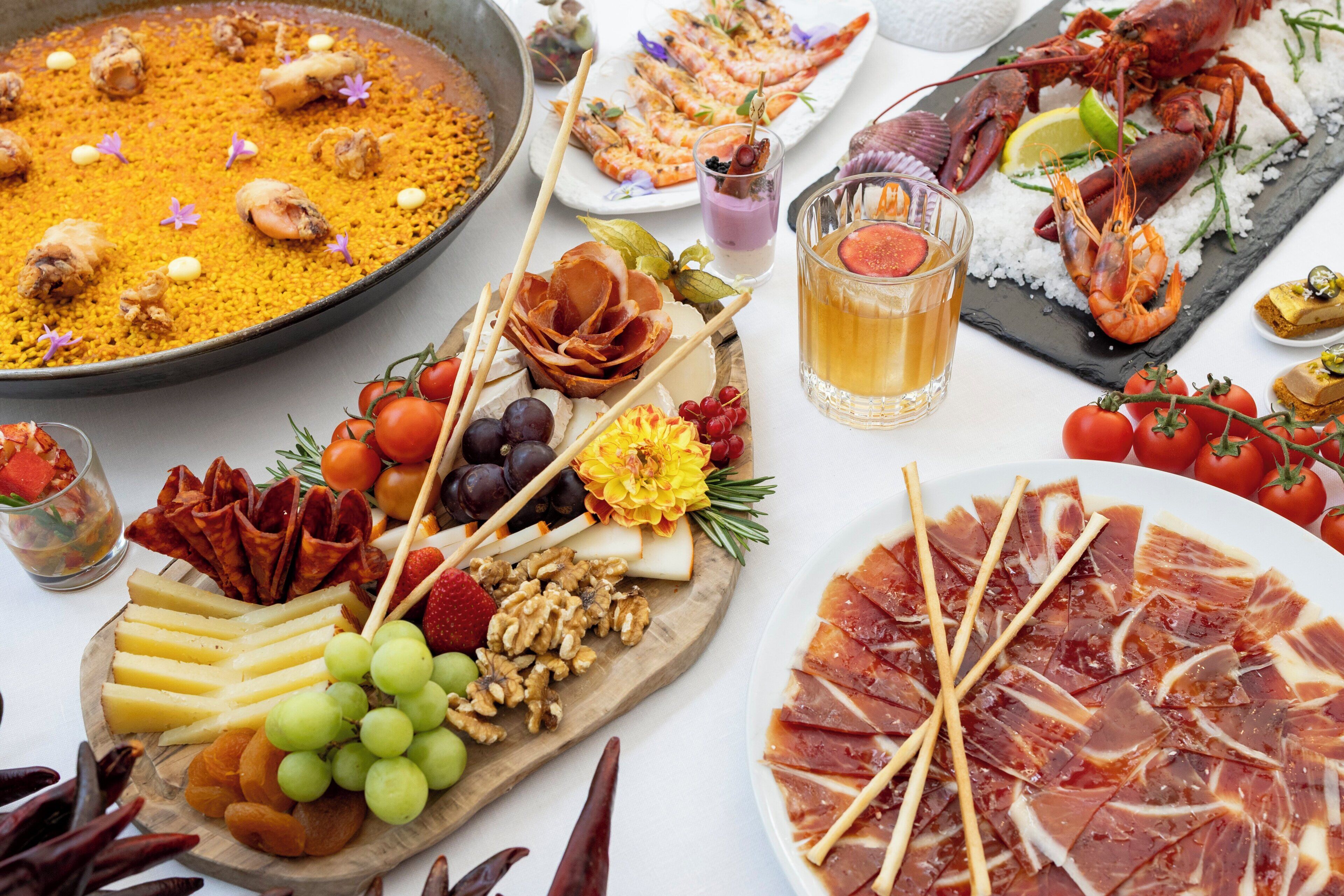 Diversos alimentos, incluyendo un gran plato de arroz, una selección de carnes, quesos y frutas.