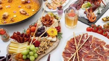 Diversos alimentos, incluyendo un gran plato de arroz, una selección de carnes, quesos y frutas.