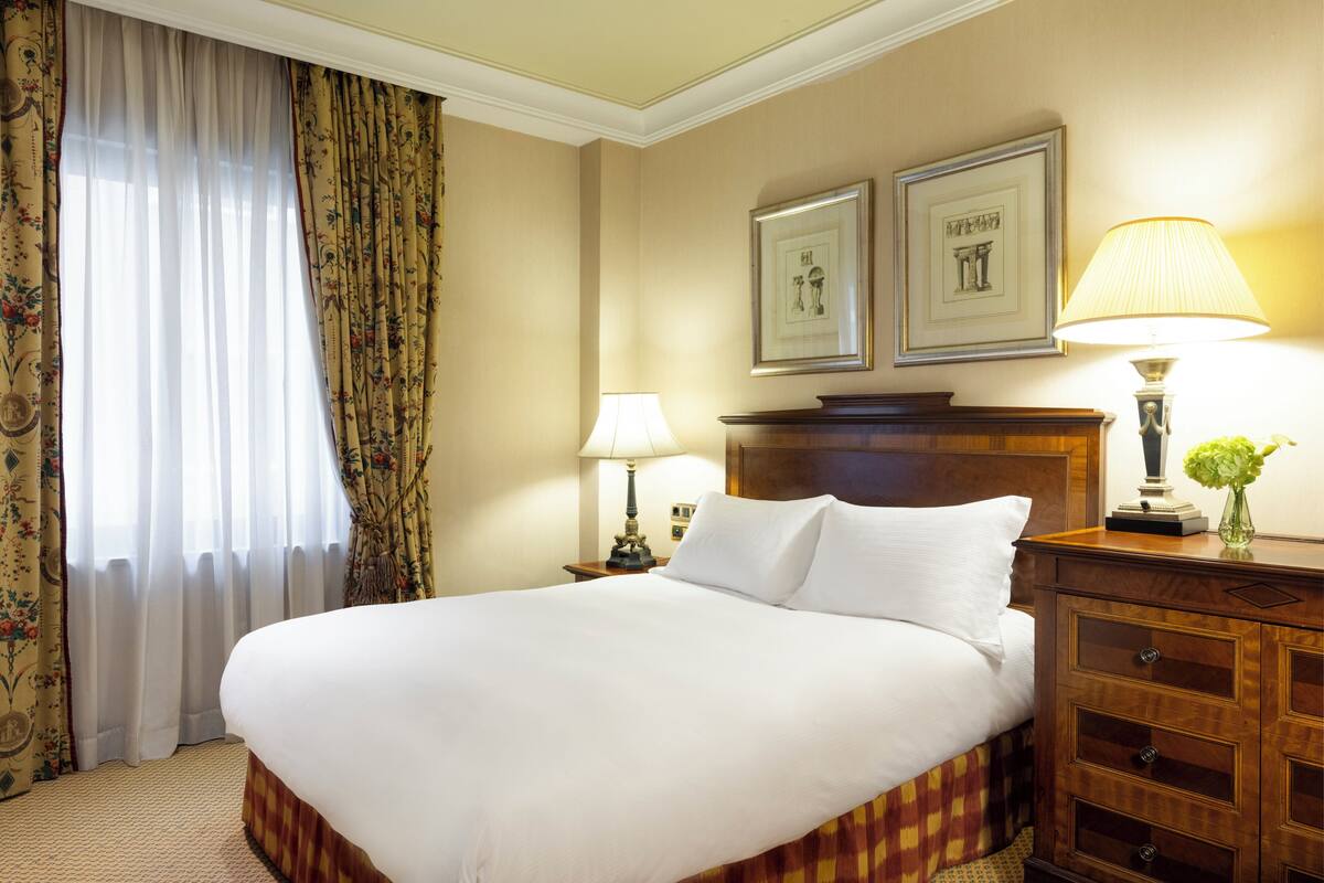 Una habitación de hotel con una cama grande, dos lámparas de noche, una mesita de noche de madera y un aparador.