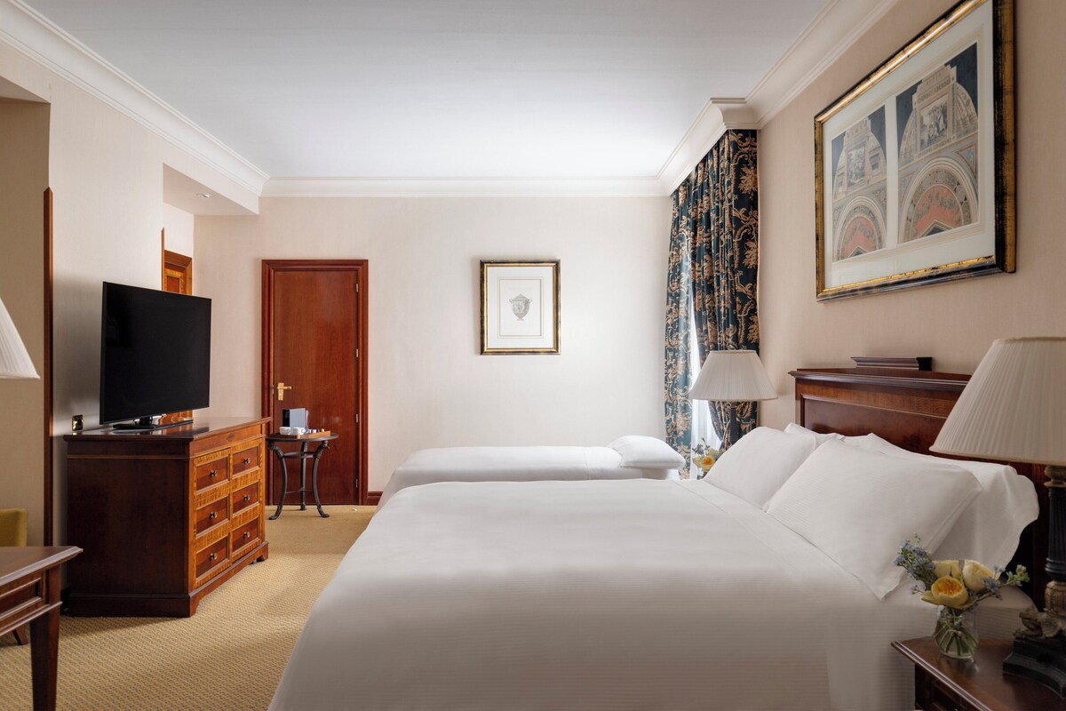 Habitació d'hotel amb un llit gran, televisió, un taulell i un quadre al mur.