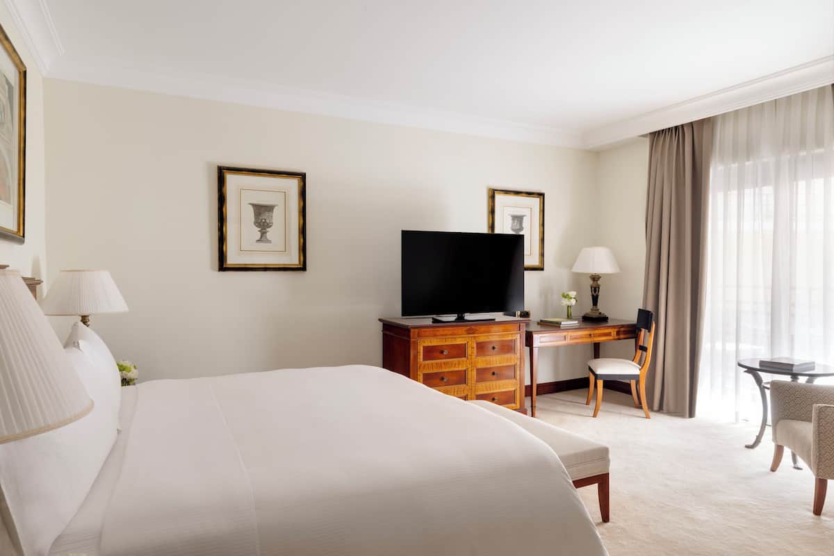 Una habitación de hotel con una cama grande, un escritorio con televisor, una silla y una mesita.
