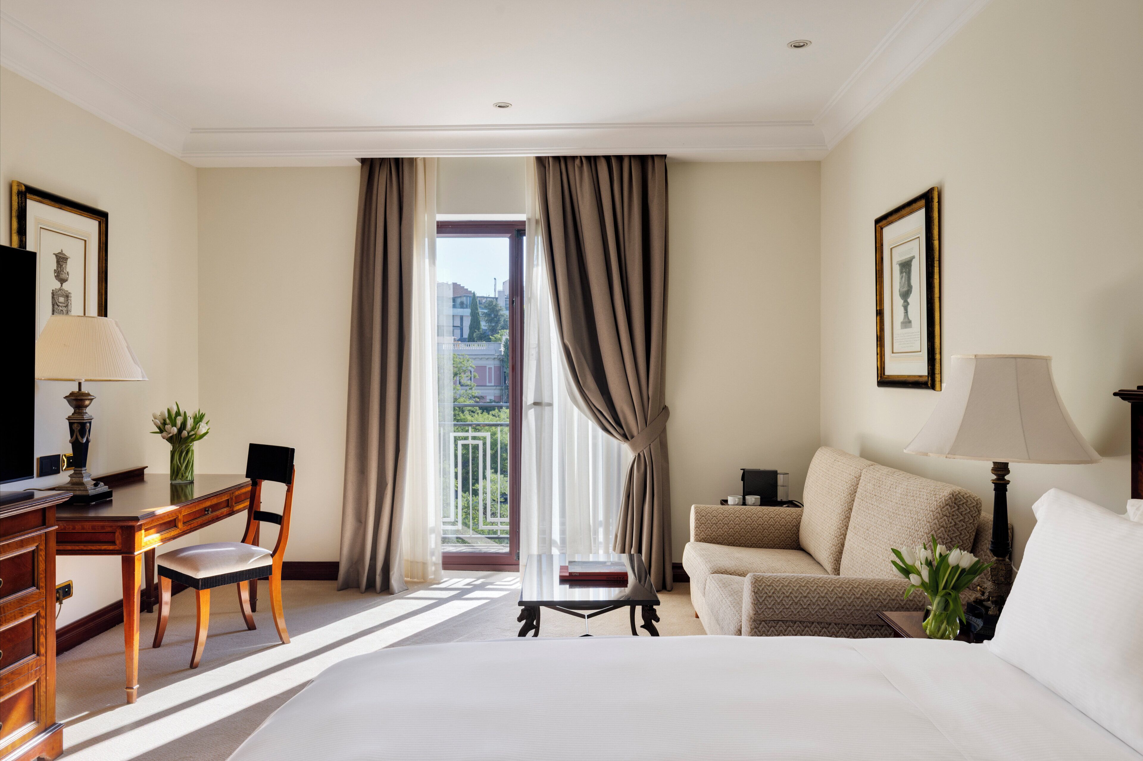 Une chambre d’hôtel comprenant un lit, un bureau avec une chaise, un canapé et un balcon avec des rideaux.