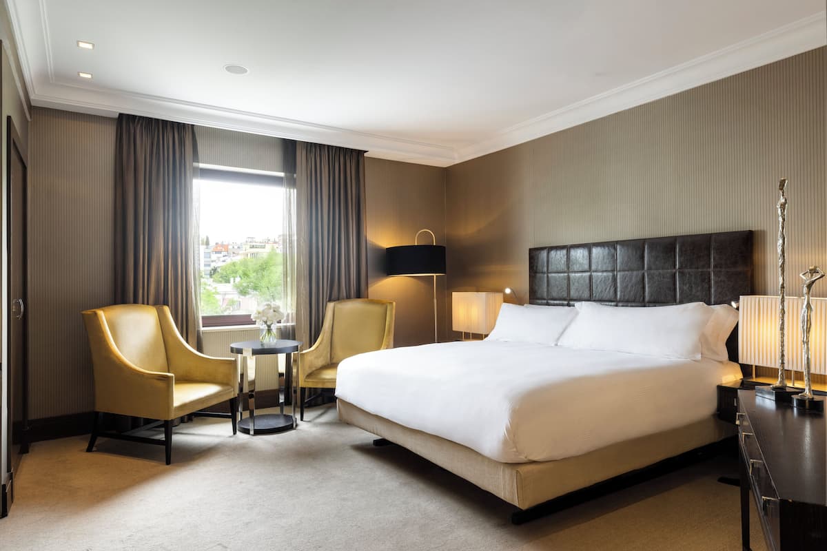Una habitación de hotel con una cama grande, dos sillas, una mesita y una lámpara.