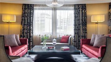 Habitación de hotel con sofá rojo, una mesita de centro de vidrio y vistas a través de amplias ventanas con cortinas.