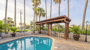 Un área de piscina con una pérgola, sillones reclinables y plantas en macetas.