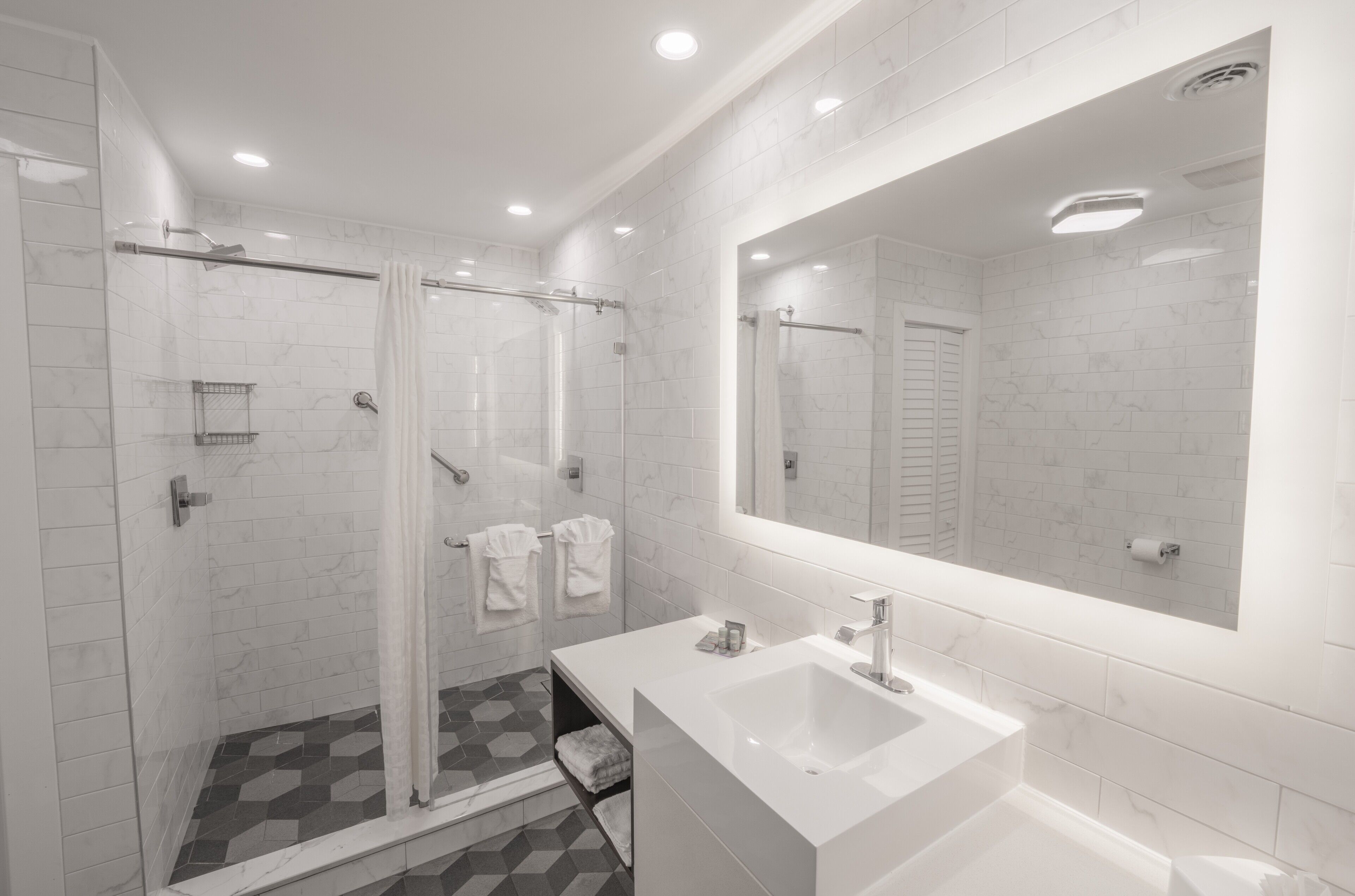 A modern bathroom with a glass shower enclosure, a large mirror, and a white sink.